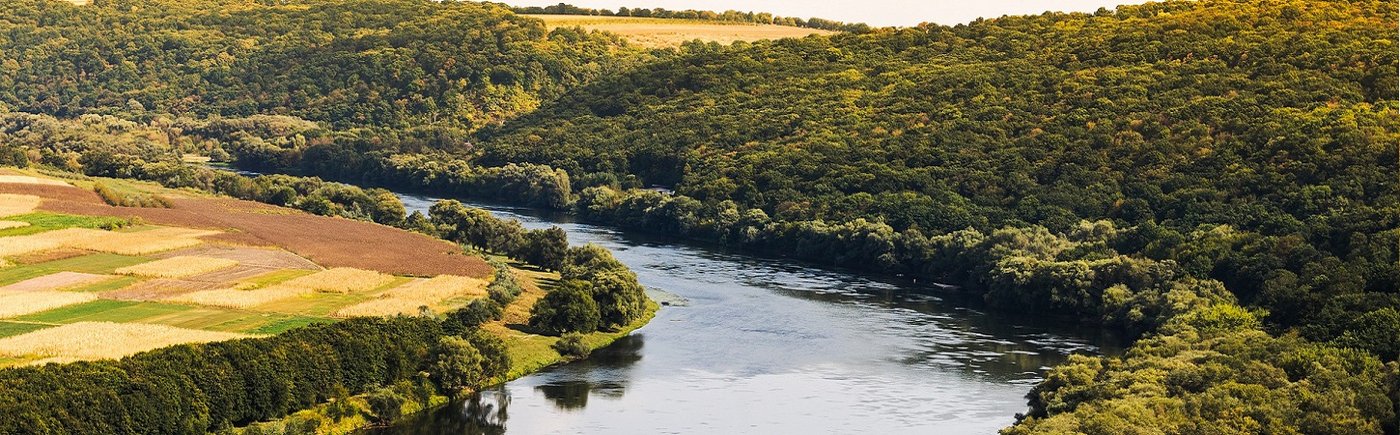 Das Bild zeigt einen Fluss in Moldawien, der von Wald und Feldern umgeben ist.